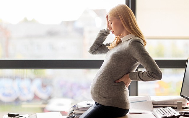 Eine Schwangere Frau im Office, die sich mit der Hand am Kopf hält