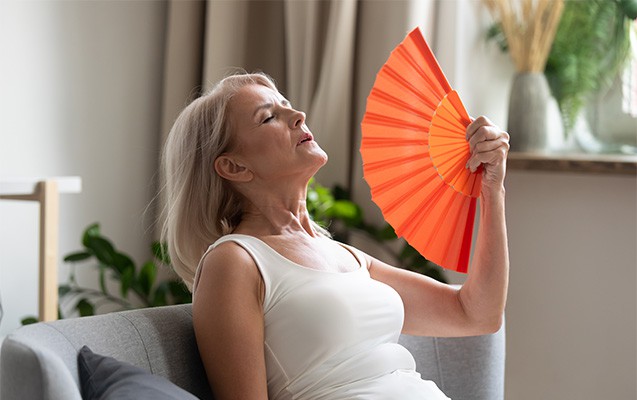 Eine sitzende Frau fächert sich mit einem Fächer Luft zu.